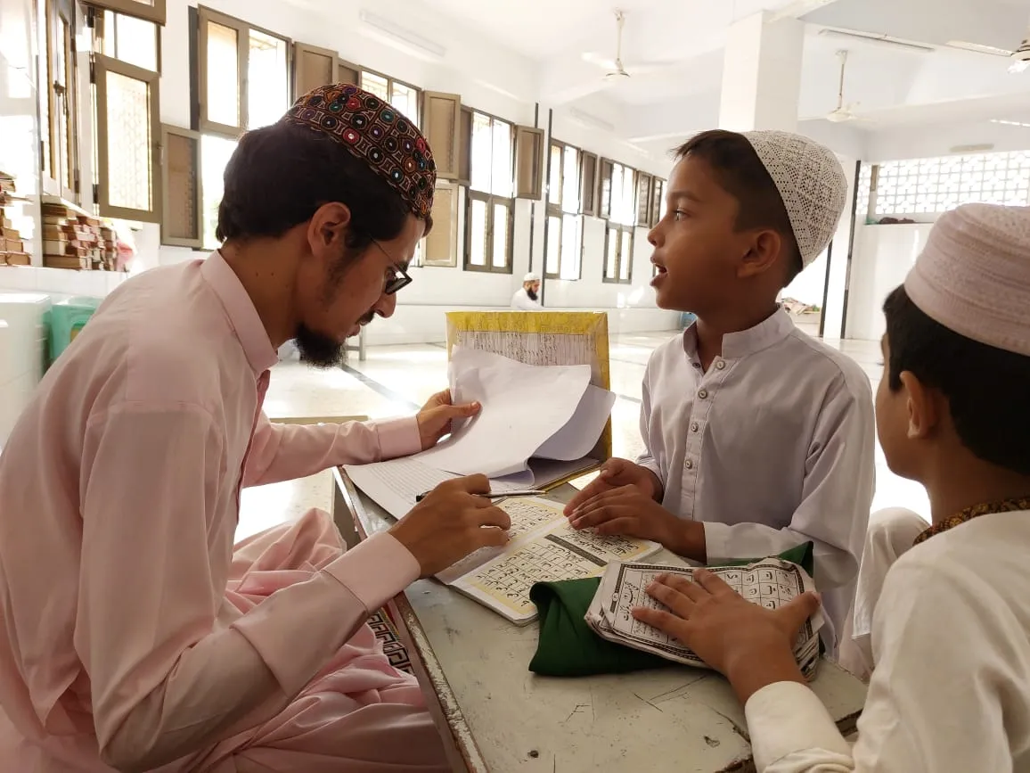 A teacher checking Qaida lessons with young students